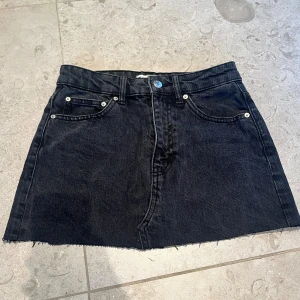 Svart jeanskjol från Perfect Jeans - Säljer en svart jeanskjol från Perfect Jeans i storlek 34. Kjolen är kort med rå kant nertill, klassiska femficksdetaljer och dragkedja framtill. Perfekt för dig som gillar en enkel och stilren look med denimkänsla.