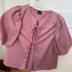 Rosa blus med puffärm från Gina Tricot - Supersöt rosa blus från Gina Tricot med puffiga korta ärmar och två knytningar framtill. 