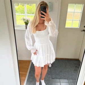Vit kort klänning med smock och volang - Superfin vit kort klänning från Bikbok med smockad överdel, långa puffärmar med broderade detaljer och volangig kjol. Klänningen har fyrkantig ringning och är perfekt för en fräsch och somrig look. Storlek xs. Helt oanvänd med prislapp kvar
