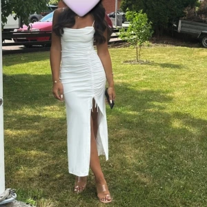 Vit långklänning med slits strl. S/XS - Säljer en snygg vit långklänning med draperad överdel och rynkade detaljer framtill. Klänningen har en hög slits som ger en extra touch och smala axelband. Perfekt för dig som vill sticka ut med en stilren look.