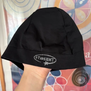 Svart mössa från Starlight - En svart, enkel och stilren mössa från Starlight med logga framtill i grått. Mössan är tillverkad i mjuk bomull och har en klassisk passform som sitter skönt på huvudet. Perfekt för att hålla värmen och ge en clean look. Priset går självklart att diskutera!