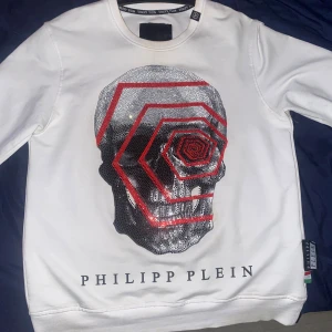 Vit Philipp Plein sweatshirt (äkta) - Säljer en vit sweatshirt från Philipp Plein med en stor glittrig dödskalle framtill och röda grafiska detaljer. Tröjan har rund hals, långa ärmar och coola logodetaljer. Tillverkad i bomull och polyester för en skön känsla. Självklart äkta! Storlek XL men skulle säga passat mer ifall man har storleken L                      Nypris : 1100€.                                                        Mitt pris : 4000kr priset går att diskuteras!