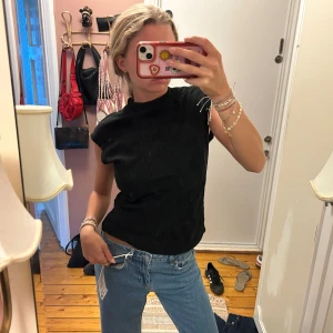 Svart ribbad ärmlös topp - Säljer en svart ribbad topp med hög hals och ärmlös design. Toppen har en clean och enkel look som passar perfekt till jeans eller kostymbyxor. Materialet är mjukt och stretchigt för en bekväm passform.