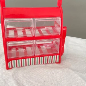 Röd liten godishyllan med lådor - Söt godishylla röd plast med fyra genomskinliga lådor och randig detalj längst ner. Perfekt för att organisera små sminkprylar som läppstift, ögonskuggor eller borstar. Kommer med en liten röd pincett i plast.