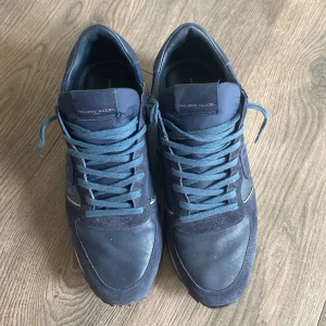 Philippe Model blåa - Snygga mörkblå sneakers från Philippe Model med ovandel i mocka och skinn, samt detaljer i textil. Skorna har rund tå, snörning och en vit platt sula som ger en sportig vibe. Nypris ligger på 3299 de är använda några gånger så de är i riktig bra skick rekomenderas storlek 45.