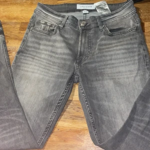 Grå skinny jeans från Smog/Denim - Snygga grå jeans från Smog/Denim i storlek 28/30. Modellen är skinny med klassisk femficksdesign och dragkedjegylf. Jeansen har en tvättad look med ljusare partier och är tillverkade i stretchigt denim för en tight passform.