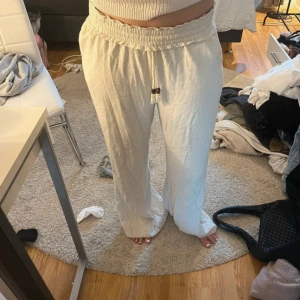 Vita linnebyxor med snörning - Säljer ett par ljusa, vida linnebyxor med resår och snörning i midjan. Byxorna har en avslappnad passform och är perfekta för varma dagar. Snygga trädetaljer på snöret ger en extra touch. Superbekväma och luftiga!