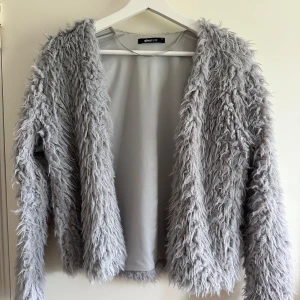 Ljusgrå pälsjacka från Gina Tricot - Säljer en fluffig och supermjuk ljusgrå pälsjacka från Gina Tricot. Jackan har lång ärm och öppen front, perfekt för dig som vill sticka ut med en cozy vibe. 