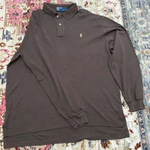 Långärmad pikétröja Polo Ralph Lauren - Säljer en brun långärmad pikétröja från Polo Ralph Lauren i storlek L. Tröjan har klassisk krage, två knappar och den ikoniska broderade loggan på bröstet. Tillverkad i mjuk bomull, perfekt för dig som gillar stilren och enkel design.