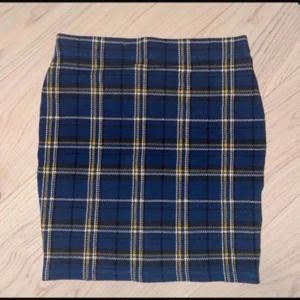 Blå rutig kortkjol - Supersnygg blå kortkjol med rutigt mönster i gult och vitt. Kjolen har en rak och tight passform som ger en cool och trendig vibe. Perfekt att matcha med en stickad tröja eller skinnjacka för en stilren look.