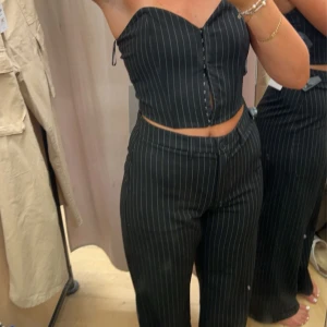 Svarta randiga kostymbyxor och corsett topp till - Snygga svarta kostymbyxor med vita tunna ränder. Byxorna har en rak passform och normal midja, vilket ger en chill och stilren look. Till den säljer jag en corsett top som gör en perfekt arbeta outfit eller fest outfit. Säljer båda i ett. 