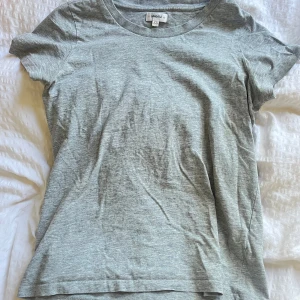Grå t-shirt från Crocker XS - En enkel och stilren grå t-shirt från Crocker i storlek XS. T-shirten har rund hals och korta ärmar, perfekt för en chill och avslappnad look. Materialet är mjuk bomull som känns skönt mot huden. Passformen är normal och funkar till allt.