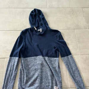 Blåmelerad hoodie från H&M - Snygg hoodie från H&M i tvådelad design med mörkblå ovandel och blåmelerad nederdel. Tröjan har huva, långa ärmar och är stickad i mjukt material. Perfekt för dig som gillar en chill och stilren look.
