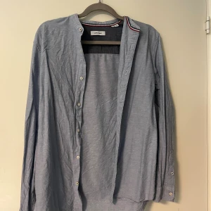 Ljusblå henley-skjorta Jack & Jones - Säljer en ljusblå henley-skjorta från Jack & Jones i storlek S. Skjortan har lång ärm, knappar framtill och en enkel, stilren design med en tunn randig detalj på insidan av kragen. Tillverkad i mjuk bomull som känns skön mot huden.