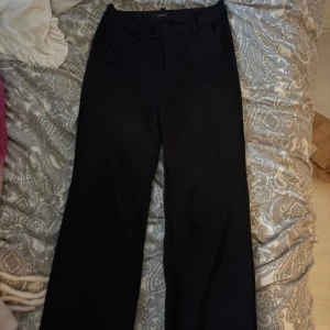 Svarta kostymbyxor från Vero Moda -  svarta kostymbyxor från Vero Moda i rak modell. Byxorna har fickor fram, bälteshällor och stängs med dragkedja och knapp. Perfekta till en snygg och stilren look.