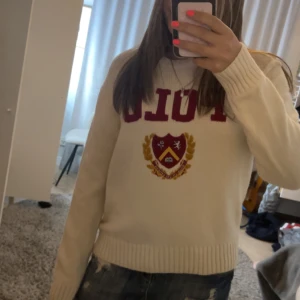 Vit stickad tröja Polo Ralph Lauren - Vit stickad tröja från Polo Ralph Lauren med röd POLO-text och broderat emblem i rött och gult framtill. Rund hals och ribbade muddar vid ärmslut och nederkant. jättefin men har tyvärr inte kommit till användning 💕💕 