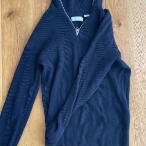 Mörkblå stickad half zip från Jack & Jones - Mörkblå ribbstickad tröja från Jack & Jones med half zip-dragkedja framtill. Tröjan har lång ärm och är tillverkad i ett mjukt stickat material som passar perfekt för kyligare dagar. Enkel och stilren design som funkar till det mesta.