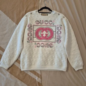 Vit quiltad Gucci sweatshirt med rosa tryck - Säljer en vit quiltad sweatshirt från Gucci med stort rosa och svart logotryck framtill.  Har kvar lappar och den är använd 1 gång                                       Nypris 19500 kr Säljer för 4000 kr vid snabb affär
