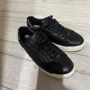 Svarta sneakers från Calvin Klein - Stilrena svarta sneakers från Calvin Klein i skinn med vita sulor. Klassisk design med rund tå, svarta snören och diskret logga på plösen. Perfekta för dig som gillar minimalistisk och clean look.