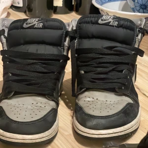 Nike Air Jordan 1 svart/grå 37.5 - Säljer ett par Nike Air Jordan 1 i svart och grått skinn med klassisk hög siluett och svart snörning. Ikonisk Nike Air-logga på plösen och vingar på hälen. Perfekta för dig som gillar streetwear och vill ha en tidlös sneaker med cool attityd. Pris går att diskutera 