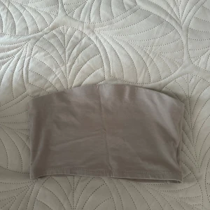 Beige bandeau tubtopp från 157 - Säljer en stilren beige bandeau tubtopp från 157 i storlek M. Toppen är ärmlös och har en enkel, clean design som är perfekt att matcha med både jeans och kjol. Mjuk och stretchig för en bekväm passform.