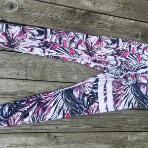 Blommiga leggings från Stronger - Snygga leggings från Stronger med blommigt mönster i lila, rosa, på vit botten . Tight passform och stretchigt material som passar perfekt till träning eller chill. Hög midja och bred resår för extra komfort.
