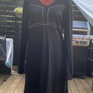 Svart långärmad klänning med nitar - Svart långärmad klänning från Zara med v-ringning och coola silvriga nitar längs byst och midja. Klänningen har dragkedja i sidan och är tillverkad i en mjuk blandning av polyester och viskos. Enkel men edgy look som sticker ut. 2 dolda sidfickor. 72% ull, 27% polyamid, 1% elastan Söm i linning har gått upp, se bild 5! Längd: 99 cm Bystvidd: 50 cm.  Inga bilder när den sitter på mig! Katter finns i hemmet! 01,S 