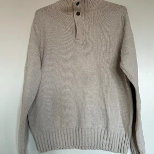 Beige stickad tröja Dressmann S - Beige stickad tröja från Dressmann i storlek M. Tröjan har hög krage med två knappar och ribbade muddar vid ärmslut och nederkant. Tillverkad i 100% bomull, perfekt för kyligare dagar. Enkel och stilren design som passar till det mesta.