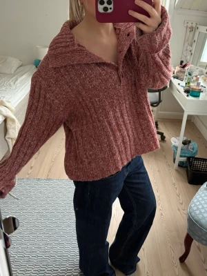 Rosa ribbstickad kofta med krage - Mysig rosa ribbstickad kofta med stor krage och knäppning framtill med fyra knappar. Tröjan har en loose passform och långa ärmar, perfekt för lager-på-lager. Materialet känns mjukt och värmande, perfekt för kyligare dagar.