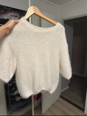 Vit fluffig stickad tröja - Supermjuk och fluffig vit stickad tröja med korta ärmar och rund hals. Tröjan har en lätt oversized passform och är perfekt för lager på lager. Den är gjord i ett gosigt material som känns lyxigt och passar till jeans eller kjol. Den har en defekt på högra bröstet som jag visat på sista bilden , tröjan kom så i nyköp men tycker inte man ser från långt håll samt märket knappt av nära. 