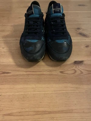 Valentino Garavani Rockrunner sneakers - Säljer ett par Valentino Garavani Rockrunner sneakers med blått och svart camouflagemönster, röda och vita detaljer på hälen samt nitar. Skorna har snörning och är tillverkade i en mix av mocka, skinn och textil. Riktigt snygga och unika sneakers för dig som vill sticka ut. Tyvärr ingår inte box och jag är även öppen för prisförslag!