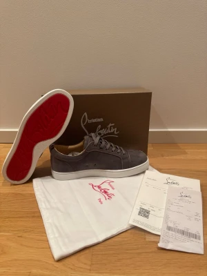 Grå mocka sneakers från Christian Louboutin - Snygga grå sneakers i mocka från Christian Louboutin med ikonisk röd sula och vita kanter. Skorna har rund tå, snörning och diskreta sömmar för en clean look. Kommer med originalkartong och dustbag. Perfekta för dig som vill ha något exklusivt och stilrent. PRISET KAN DISKUTERAS VID SNABB AFFÄR! Aldrig använda.