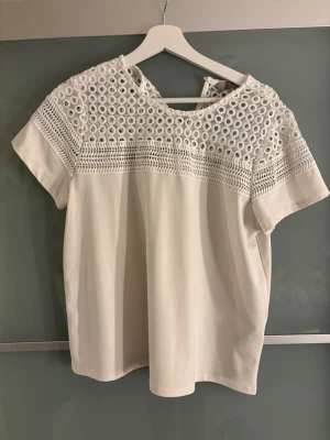 Vit blus med spets från H&M - Säljer en vit blus från H&M med korta ärmar och detaljerad spets upptill. Blusen har rund halsringning och ett snyggt hålmönster i spetsen som ger en luftig känsla. Perfekt till sommaren och enkel att styla med jeans eller kjol.❣️❣️finns ingen storlekslapp men har storlek s och skulle säga den är s/m