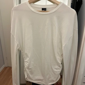 Vit långärmad topp från Gina Tricot - Säljer en enkel och stilren vit långärmad topp från Gina Tricot. Toppen har en rund halsringning och snygg rynkdetalj i sidorna som ger en cool twist till looken. 