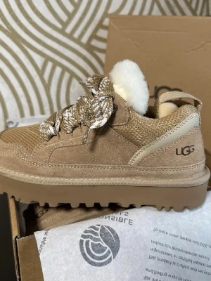 Ugg Lowmel Sand 39 - Snygga beige sneakers från UGG med grov sula och coola mönstrade snören. Skorna har ovandel i mocka och textil, samt ett fluffigt vitt ullfoder som sticker upp vid plösen. Perfekta för dig som vill ha både stil och komfort samt varma skor.Kvitto finns och fås endast via seriöst intresse. Helt nya och oanvända❤️