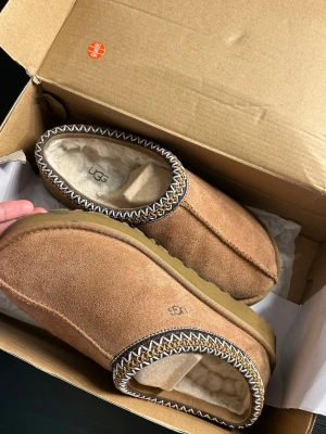 UGG mocka slip-ons med fårfoder - Bruna slip-on skor från UGG i mjuk mocka med fluffigt fårfoder. Skorna har en dekorativ kant med zigzag-Perfekta och I gott skick samt relativt nya. Skriv för mer info ☺️