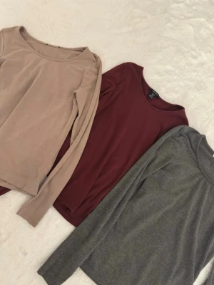 Tre långärmade toppar i olika färger - Säljer tre stilrena långärmade toppar i beige, vinröd och grå. Alla har rund halsringning och är gjorda i mjukt bomullsmaterial. Perfekta att matcha med jeans eller kjol för en enkel och snygg look. Alla tre är från New yorker.