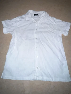 Vit kortärmad skjorta från BOSS - Vit skjorta från BOSS i storlek M. Skjortan har korta ärmar, klassisk krage och knäppning framtill. Tillverkad i ett lätt och luftigt material, perfekt för varmare dagar. Diskret BOSS-logga broderad på bröstet.