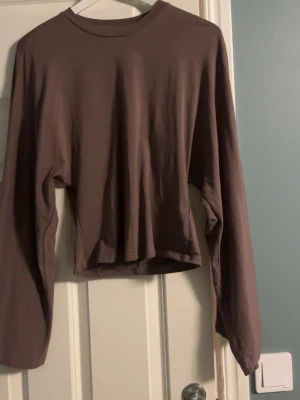 Brun croppad långärmad topp från Lager 157 - Säljer en enkel brun croppad topp med långa ärmar och rund hals. Toppen har en loose passform och är gjord i mjuk bomull, perfekt för en avslappnad stil. Passar till jeans eller kjol för en chill look.