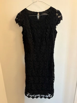 Svart spetsklänning från Esprit - Supersnygg svart kortklänning från Esprit med blommig spets och rund halsringning. Klänningen har korta ärmar och ett litet knapphål bak i nacken. Perfekt för dig som vill ha en elegant och feminin look.