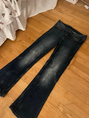 Cheap Monday Jeans - Säljer ett par klassiska cheap Monday jeans med bootcut och låg midja. Jeansen har slitningar framtill och bak, samt en grön patch på bakfickan. Tillverkade i jeansmaterial med en snygg tvättad look och femficksmodell. Storlek 29/32