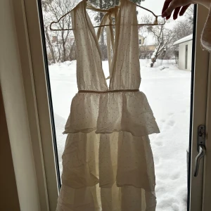 Halterneck dress - Superfin vit klänning med djup v-ringning och knyt i nacken. Klänningen har volanger i flera lager och ett diskret prickigt mönster. Perfekt för sommarens alla tillfällen och ger en romantisk vibe. Tunn och luftig i bomull.