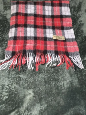 Rutig röd och svart Burberry väst - Säljer en klassisk rutig väst från Burberry i rött, svart, vitt och grått. Västen är tillverkad i 100% kashmir och har fransar längst ner. Märket syns tydligt på etiketten. Perfekt för dig som vill ha en statement piece i garderoben.