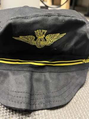 Svart tågkeps Museijärnvägen - Säljer en svart keps från Museijärnvägen Mariefred-Läggesta med gul brodyr och emblem framtill. Kepsen har gul rand runtom och text i gult. Klassisk tågkeps-look, perfekt för dig som gillar tåg eller vill ha en unik accessoar.