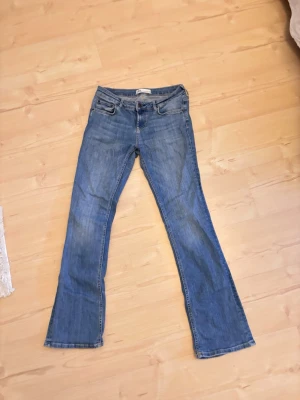 Blå bootcut jeans från Zara, strl 38 - Säljer ett par klassiska blå jeans från Zara i storlek 38. Modellen har bootcut-ben, fem fickor och normal midja. Jeansen är gjorda i bomull och har en snygg tvättad look. Perfekta till sneakers eller boots.