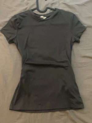 Svart kortärmad topp från H&M - En enkel och stilren svart topp från H&M med rund halsringning och korta ärmar. Modellen är figurnära och passar perfekt till jeans eller kjol. Tillverkad i mjukt och stretchigt material för en bekväm känsla.