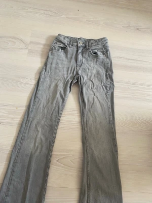 Gråa bootcut jeans - Säljer ett par gråa bootcut jeans, jeansen har en rak passform upptill och blir vidare nedtill för en snygg siluett. Materialet är mjukt jeans-tyg som är bekvämt att bära hela dagen. Storlek 158