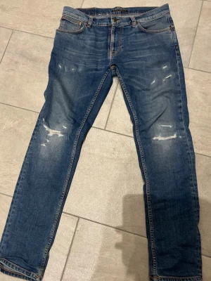 Nudie Jeans🔥 (Sale sample)🔥 - Säljer ett par Nudie Jeans Thin Finn i klassisk blå tvätt med slitningar och snyggt slitna detaljer. Jeansen har normal passform, fem fickor och är gjorda i 99% ekologisk bomull och 1% elastan för extra stretch. Perfekta för dig som gillar en avslappnad men ändå stilren look.