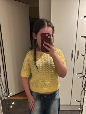 Gul stickad tröja från 157, XS - Snygg gul stickad tröja från 157 i storlek XS. Tröjan har korta ärmar och ett luftigt, hålmönstrat stickat material som känns fräscht och passar perfekt till våren och sommaren. Ribbstickade muddar vid hals, ärmslut och nederkant.
