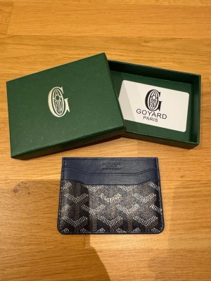 Korthållare - Säljer en stilren blå plånbok med klassiskt grafiskt mönster i vitt och svart. Insidan är gul och plånboken har flera kortfack. Perfekt för dig som vill ha något exklusivt och snyggt i fickan.